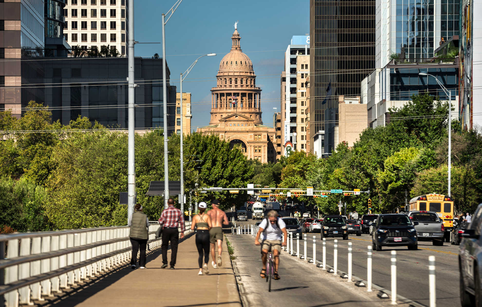 Austin, Texas, USA - November 15, 2021:  People and cars drive by the Texas State Capitol building as seen down the streets of Congress Avenue Bridge.  Austin is the state capital of Texas